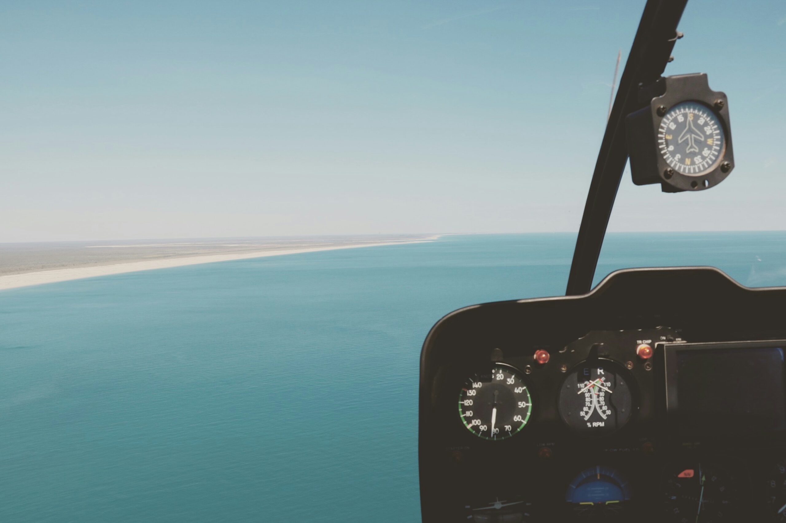 View from a helicopter cockpit over the ocean and coastline.