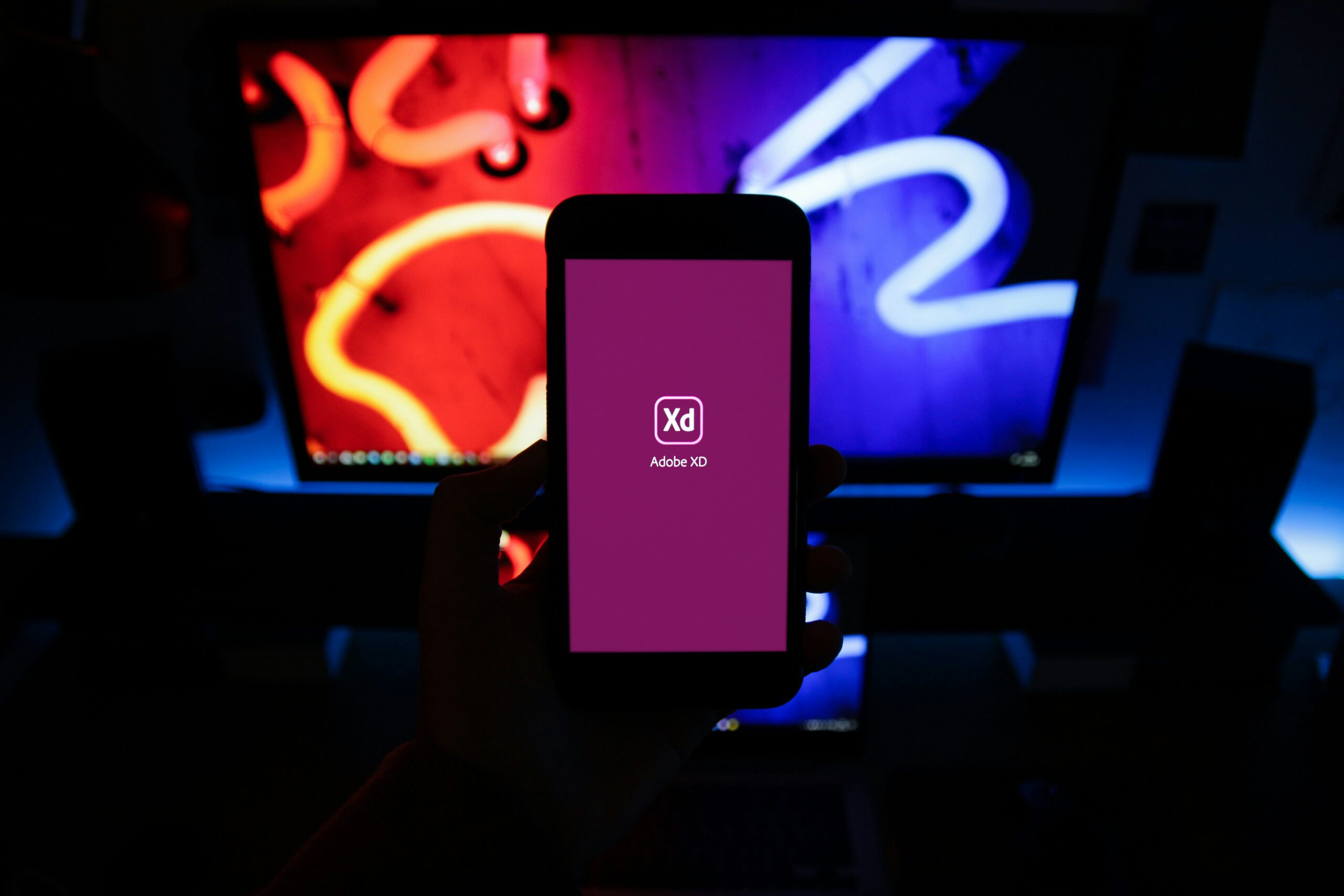Hand holding a phone with Adobe XD app, relevant to app marketing and mobile app development.