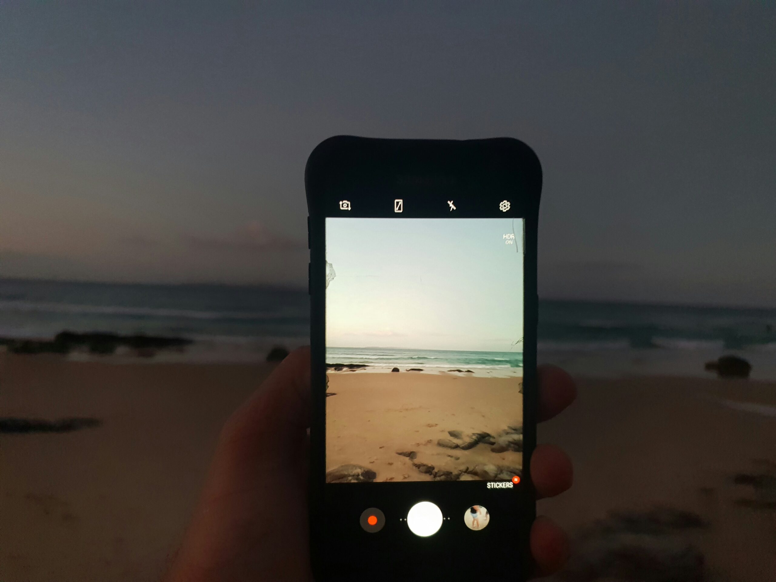 Person taking a photo with a smartphone at the beach.