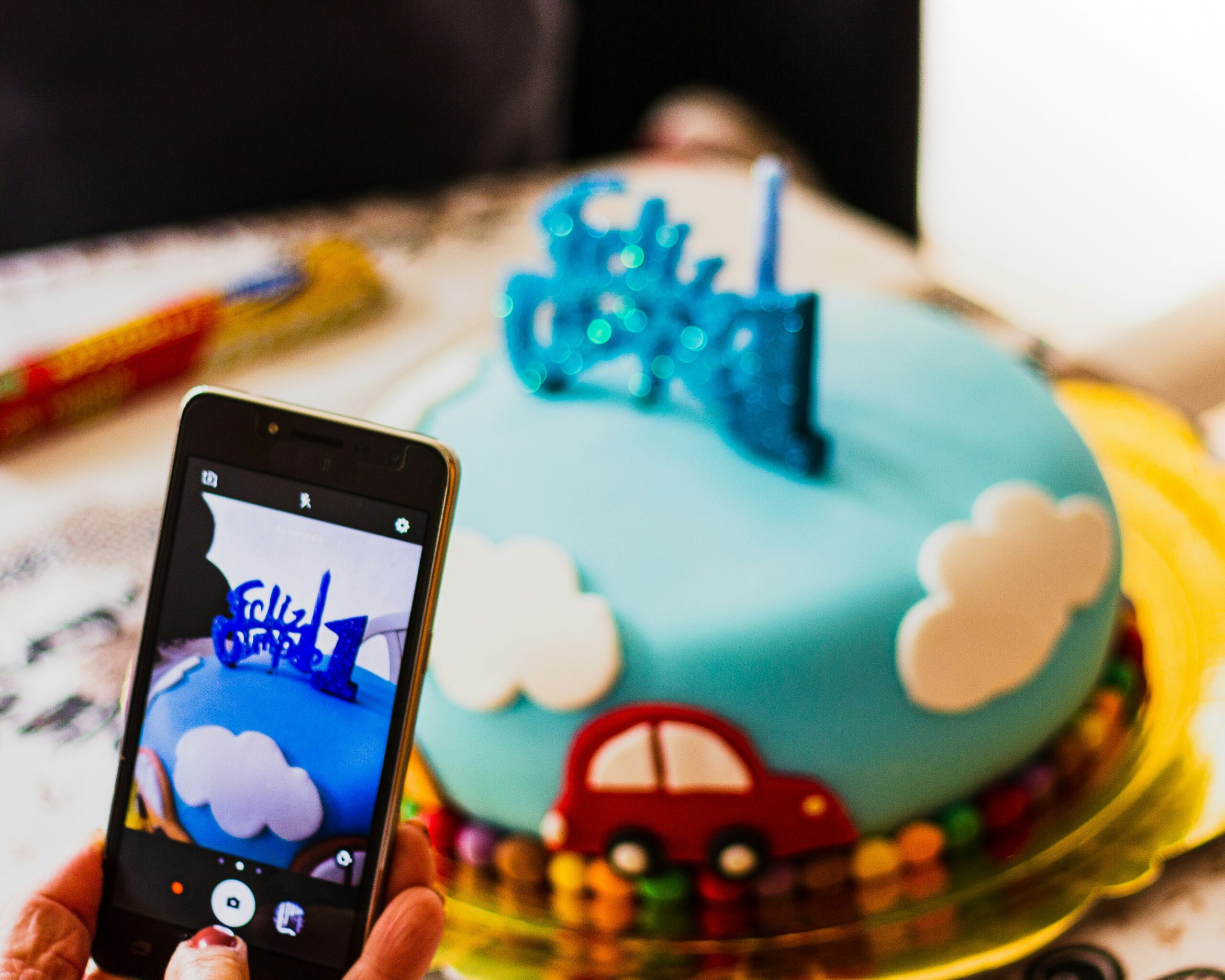 A person taking a photo of a birthday cake with a smartphone.