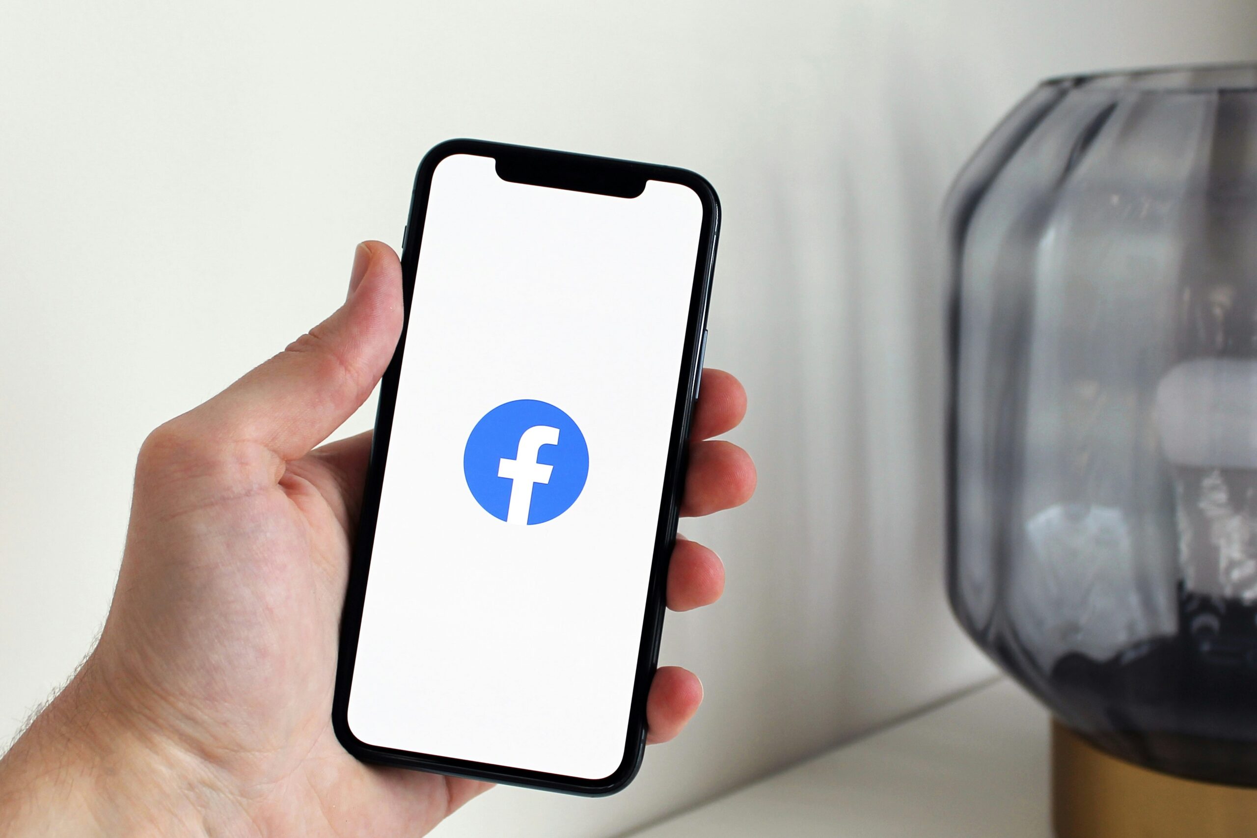 Hand holding a phone displaying the Facebook logo, for Facebook Ads and Digital Marketing.