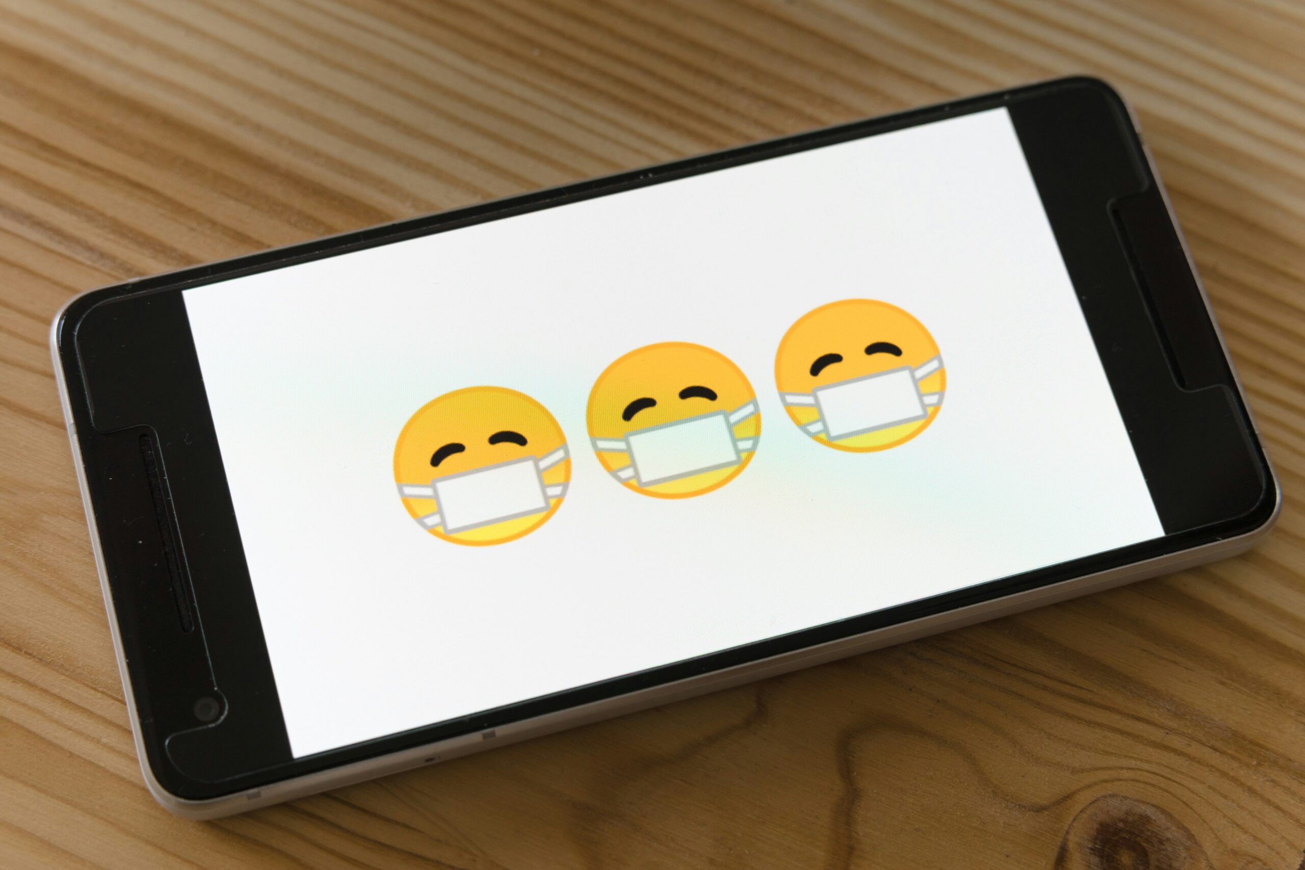 Smartphone screen displaying three masked emoji faces on a wooden table.