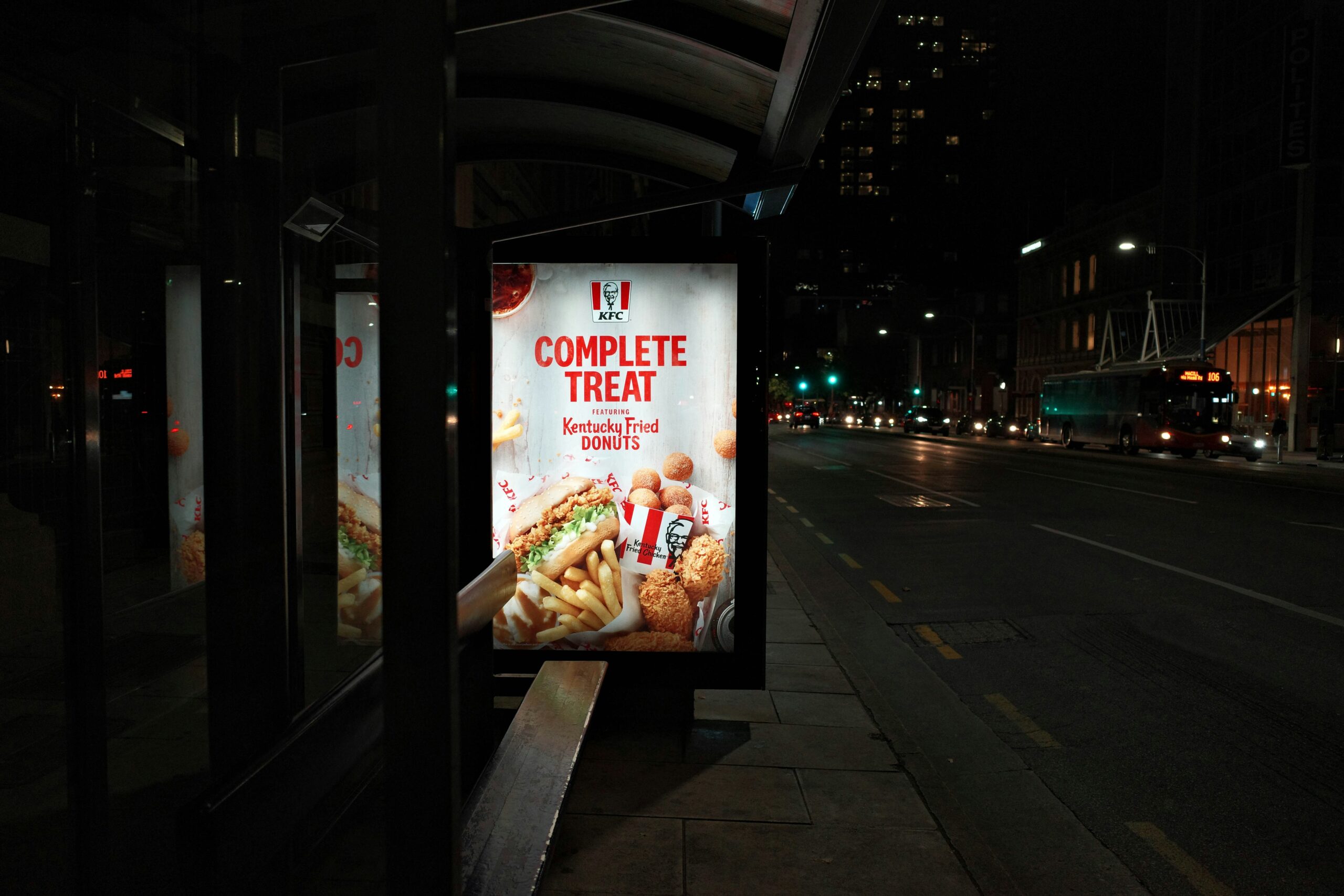 KFC advertisement at a bus stop at night, promoting a complete treat.