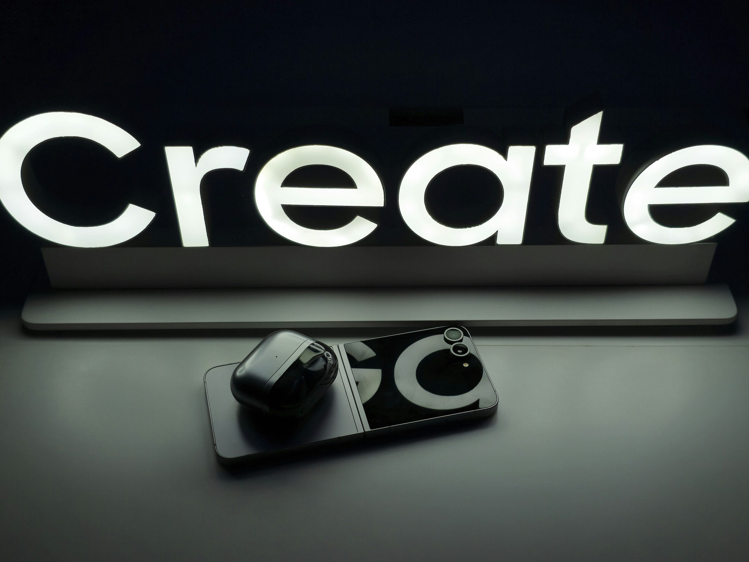 Minimalist setup with phone and earbuds, with the word 'Create'.