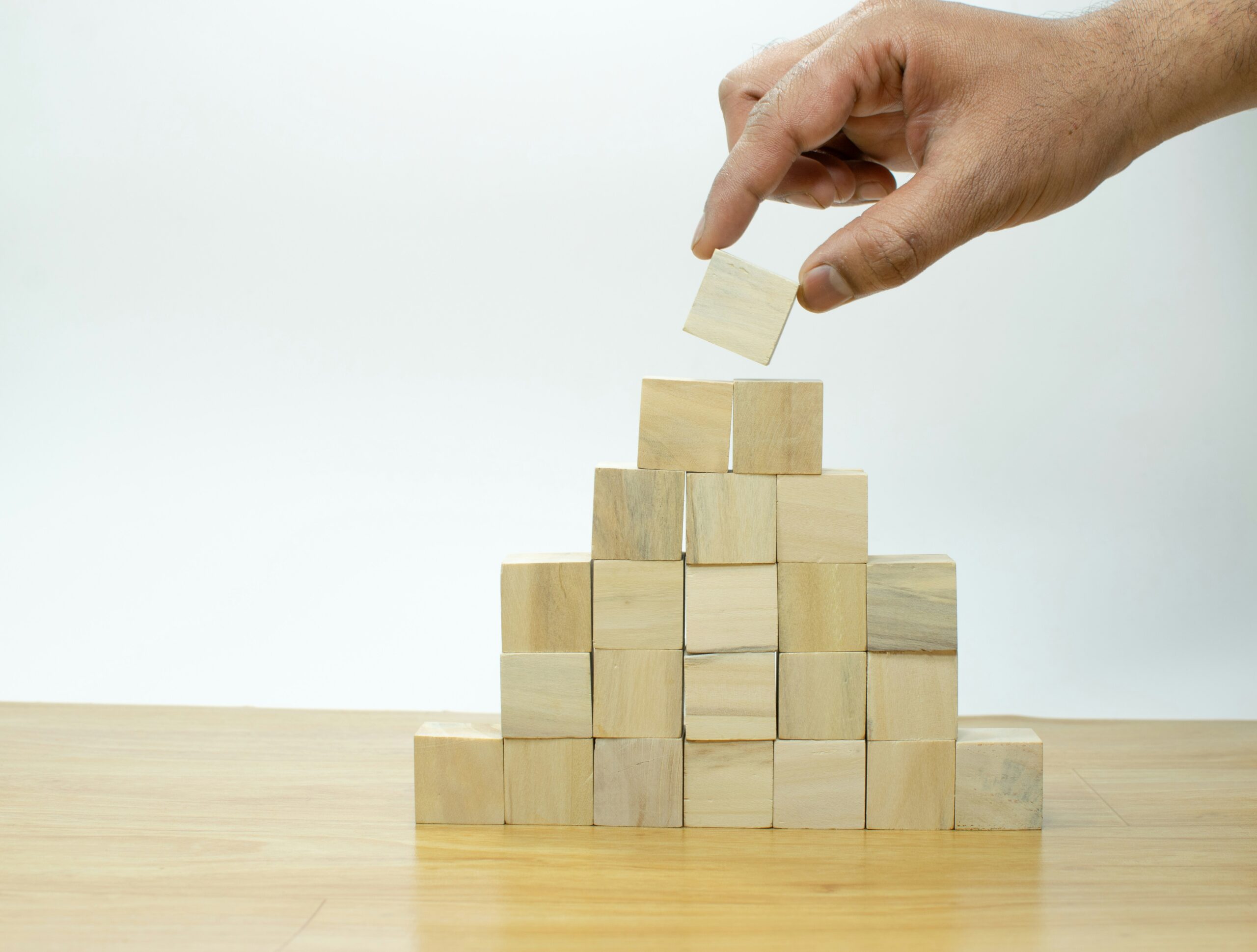 Hand placing a wooden block on a pyramid of blocks, building concept.