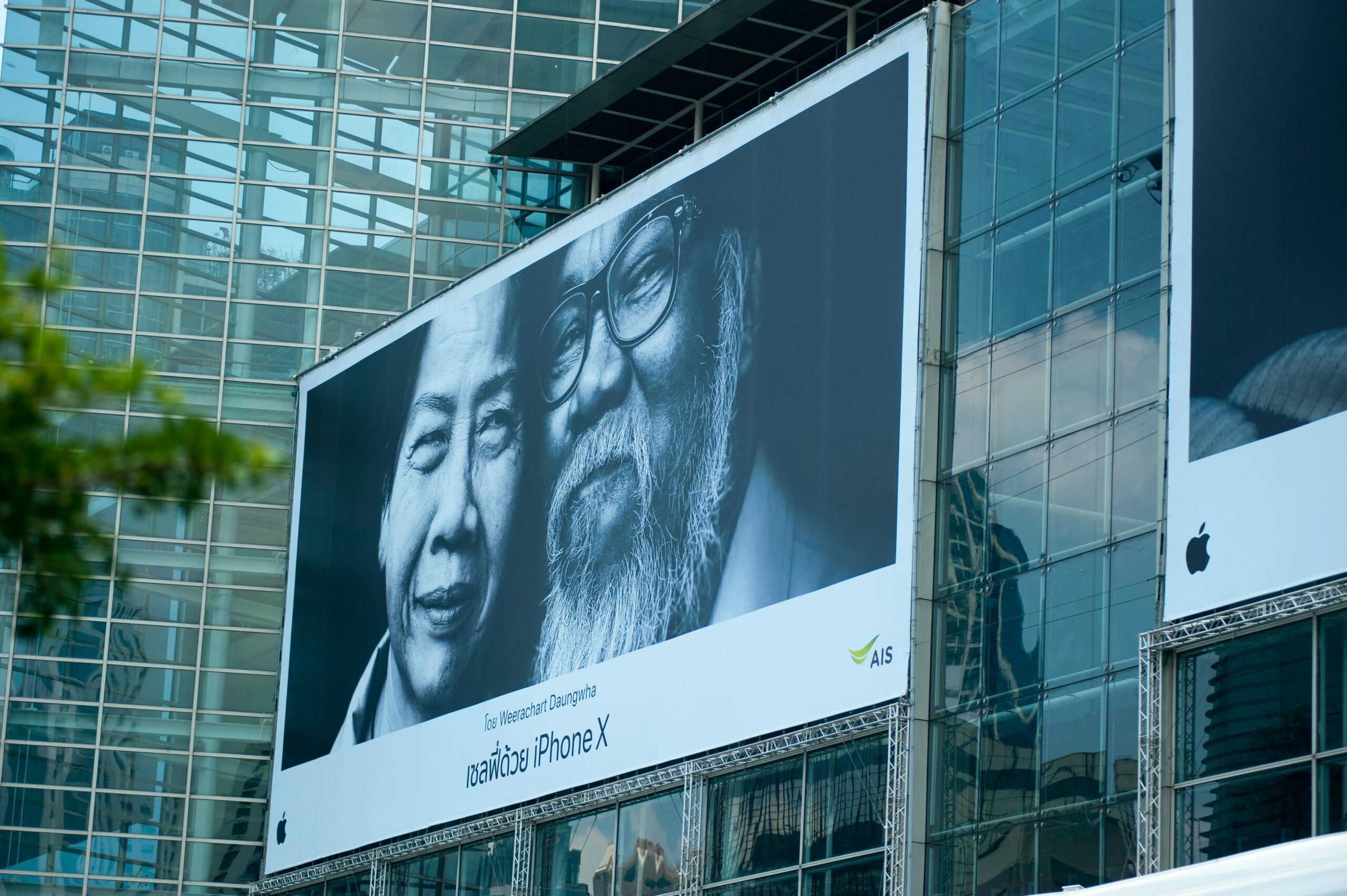 Billboard with portraits of two people, promoting an iPhone X, a form of paid advertising.