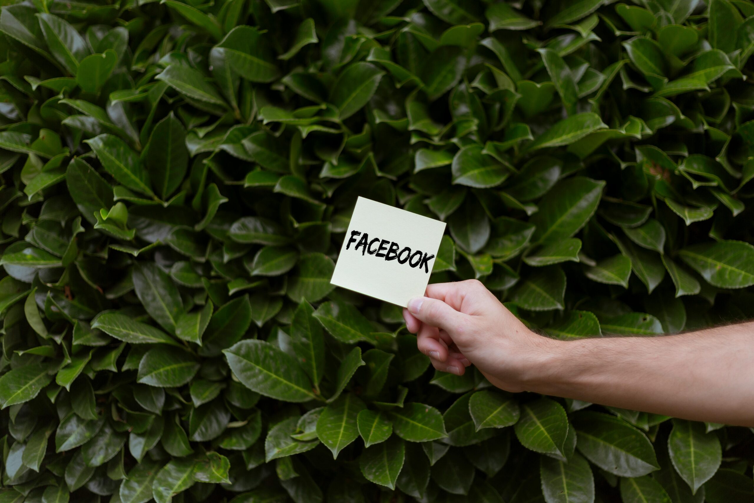 Hand holding a sticky note with the word FACEBOOK, representing social media marketing.