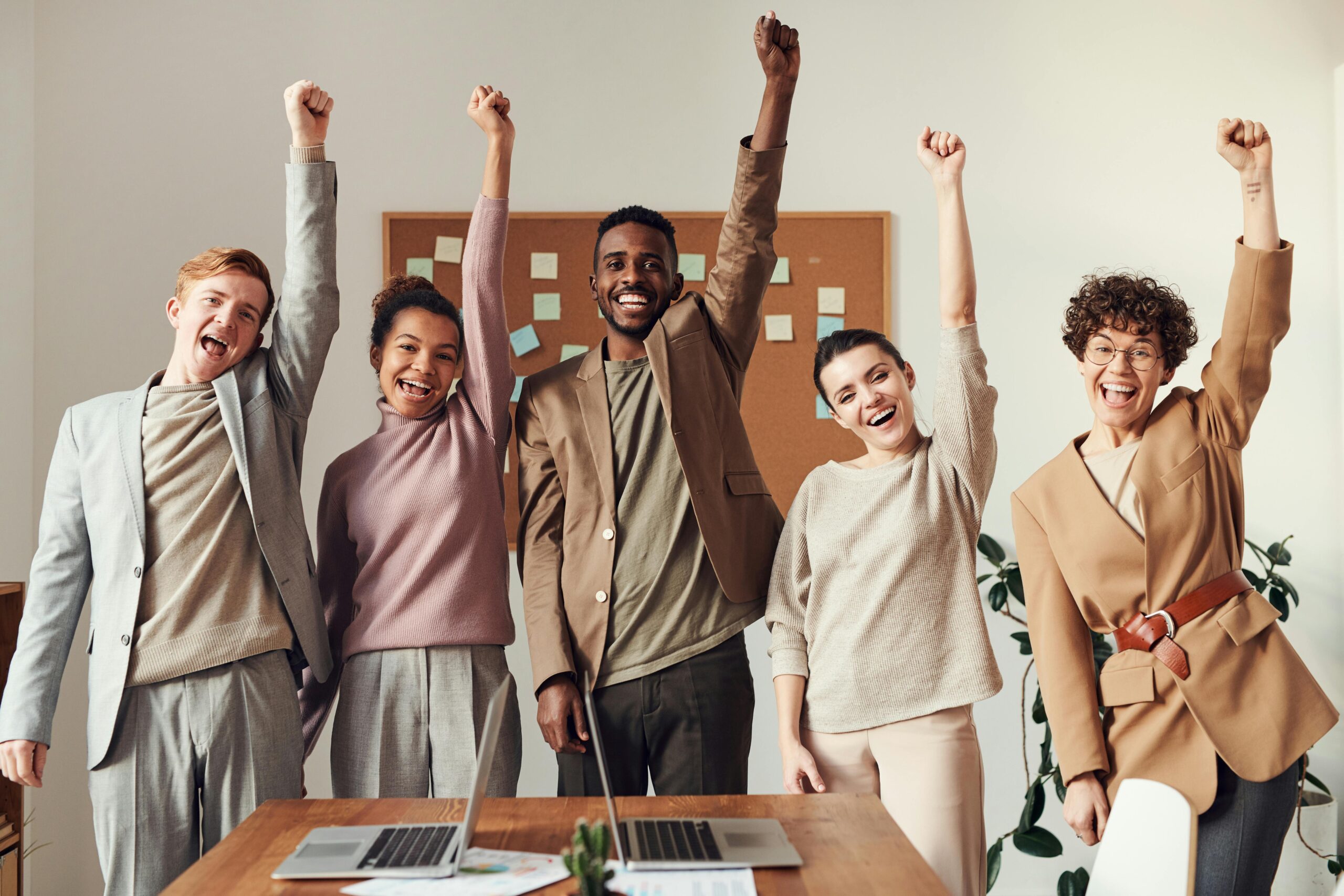 Happy diverse team celebrating success with arms raised.