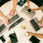 A modern office setting with diverse marketers collaborating on laptops and a large screen displaying a brand's website interface, brightly lit with natural light, showcasing teamwork and digital strategy.