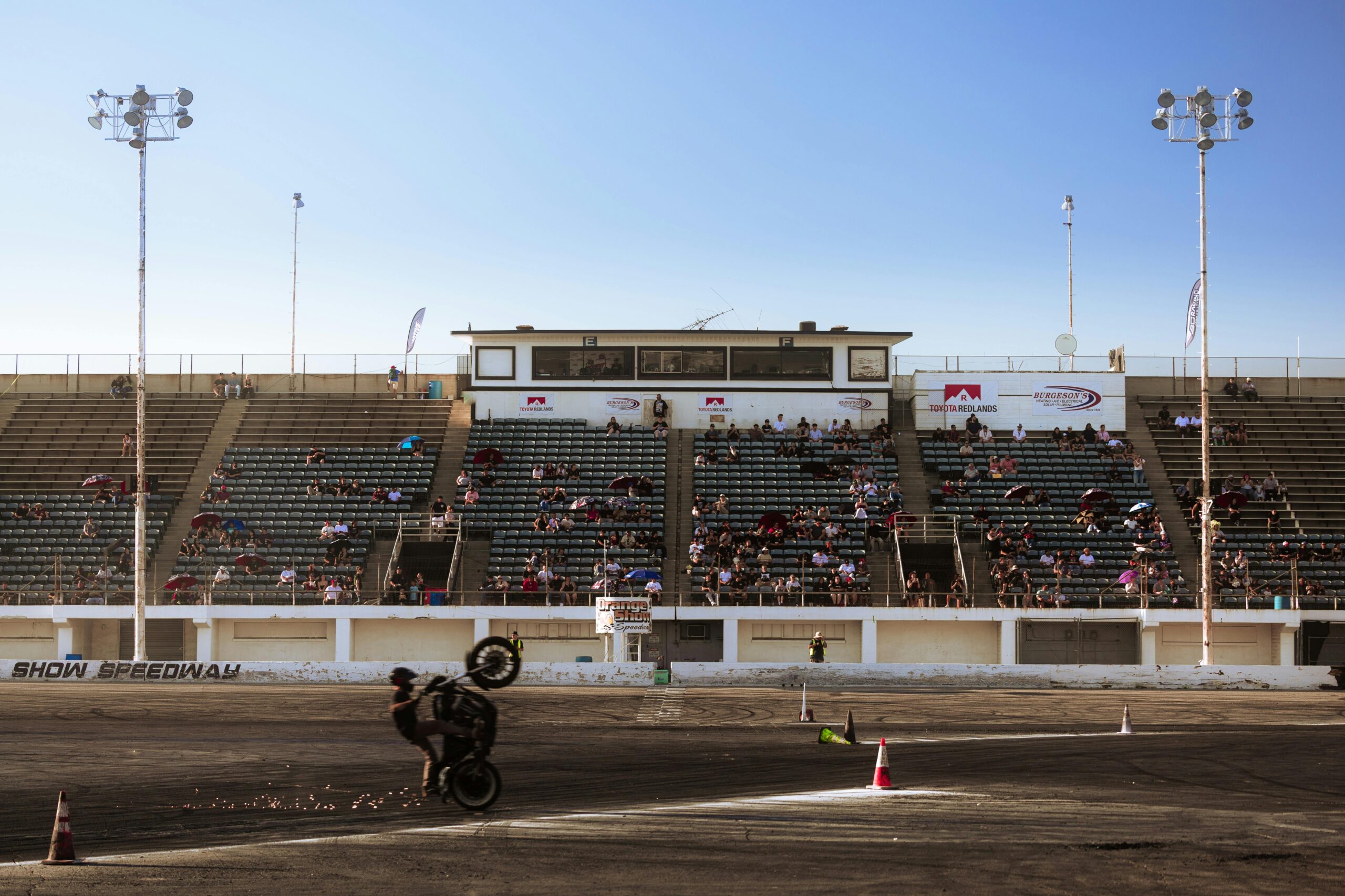 Motorcycle stunt rider performing a wheelie in a stadium.