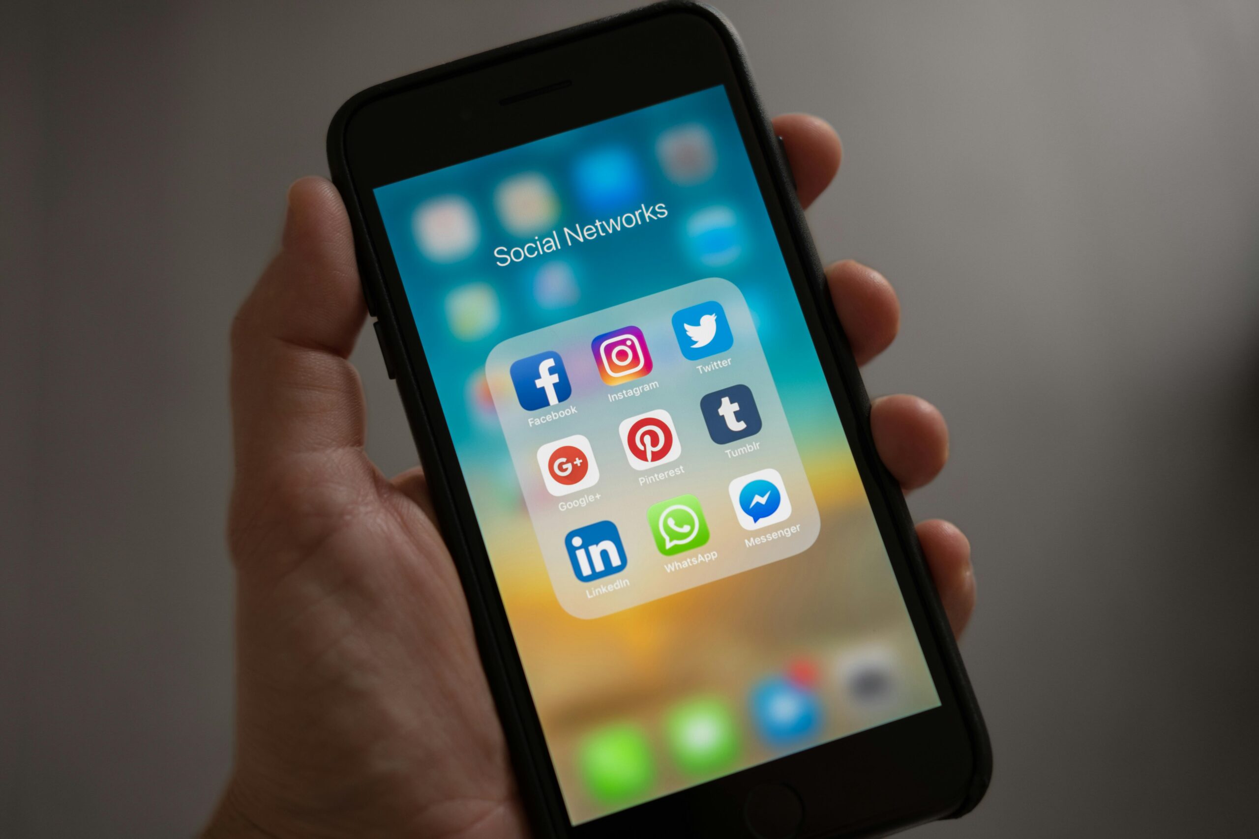 Hand holding phone showing social media app icons.