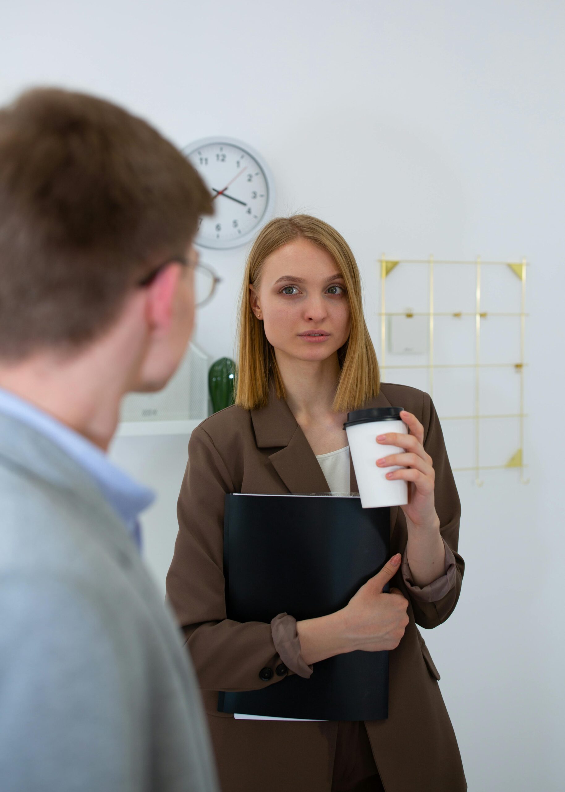 Woman in business attire holding a coffee cup, talking.