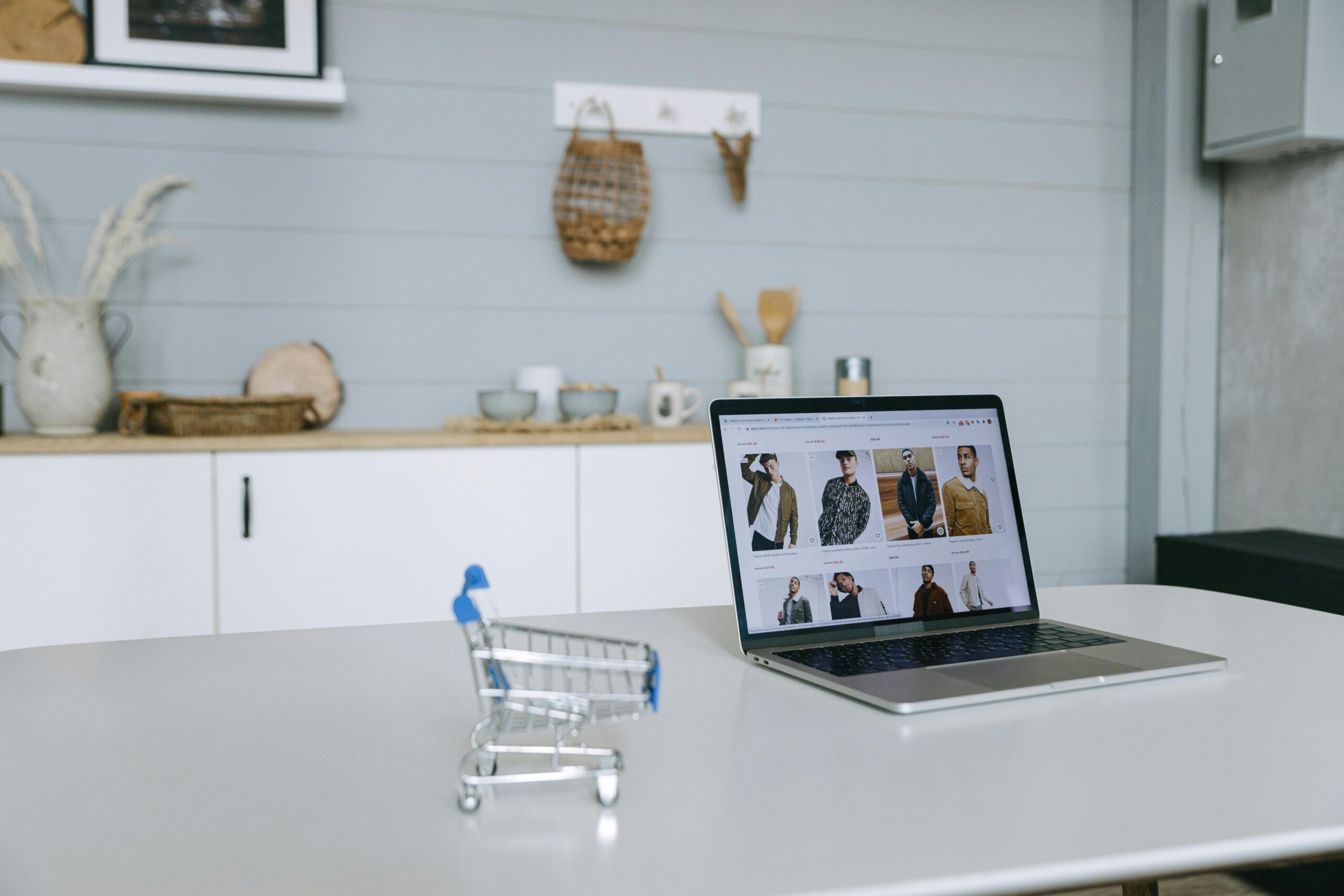 Laptop displaying online clothing store, miniature shopping cart.