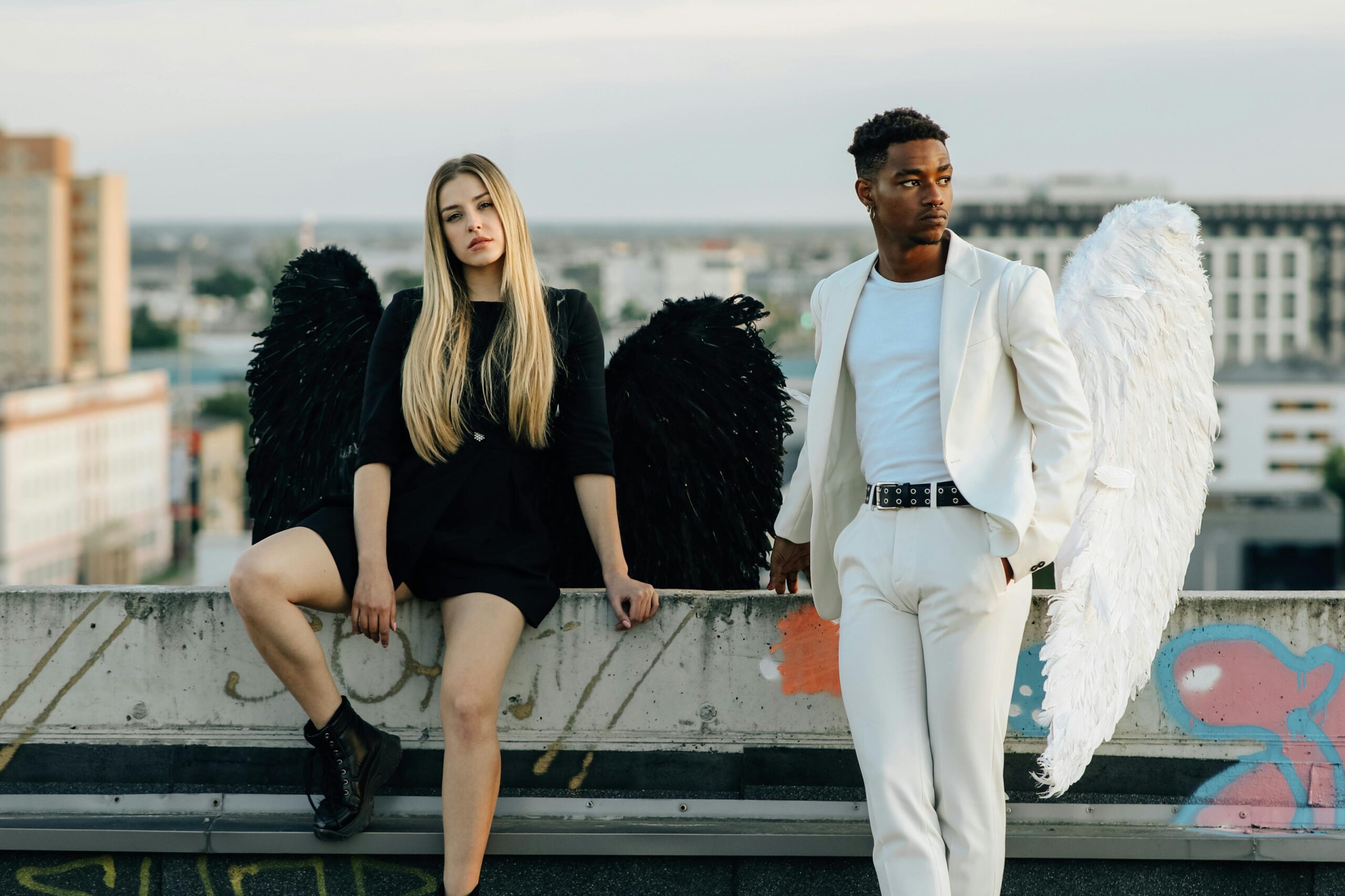 Woman with black wings and man with white wings on rooftop.