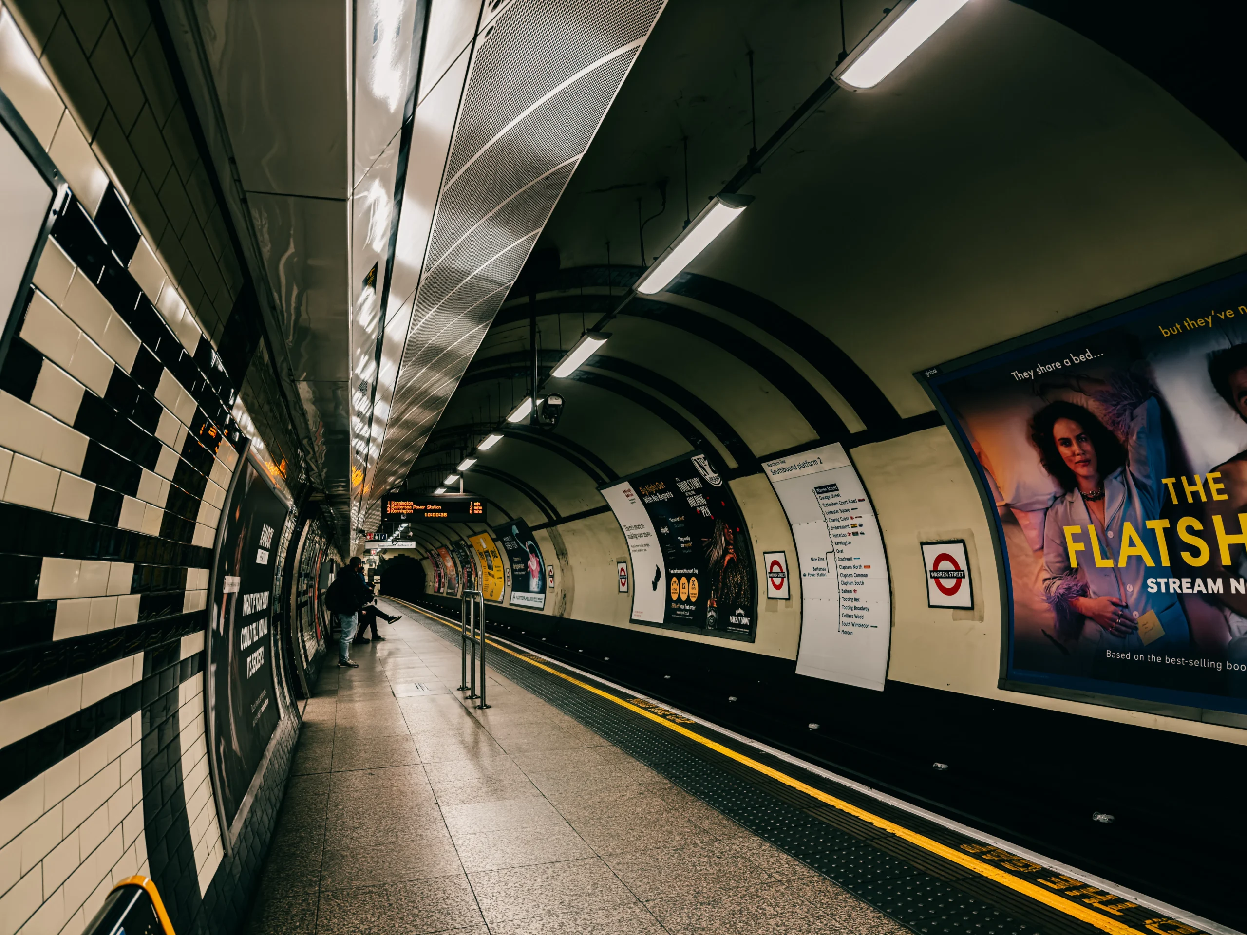 Interior view of a London Underground station platform with advertisements and signage along the walls.