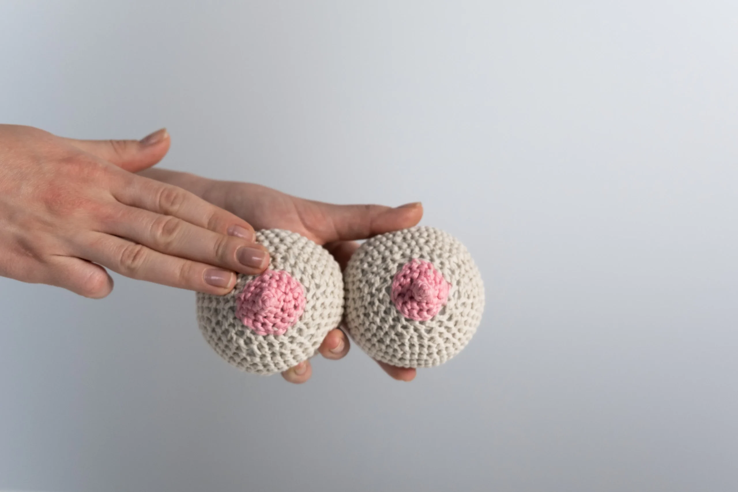 Hands holding breast cancer awareness knitted balls, promoting support and education for breast health.