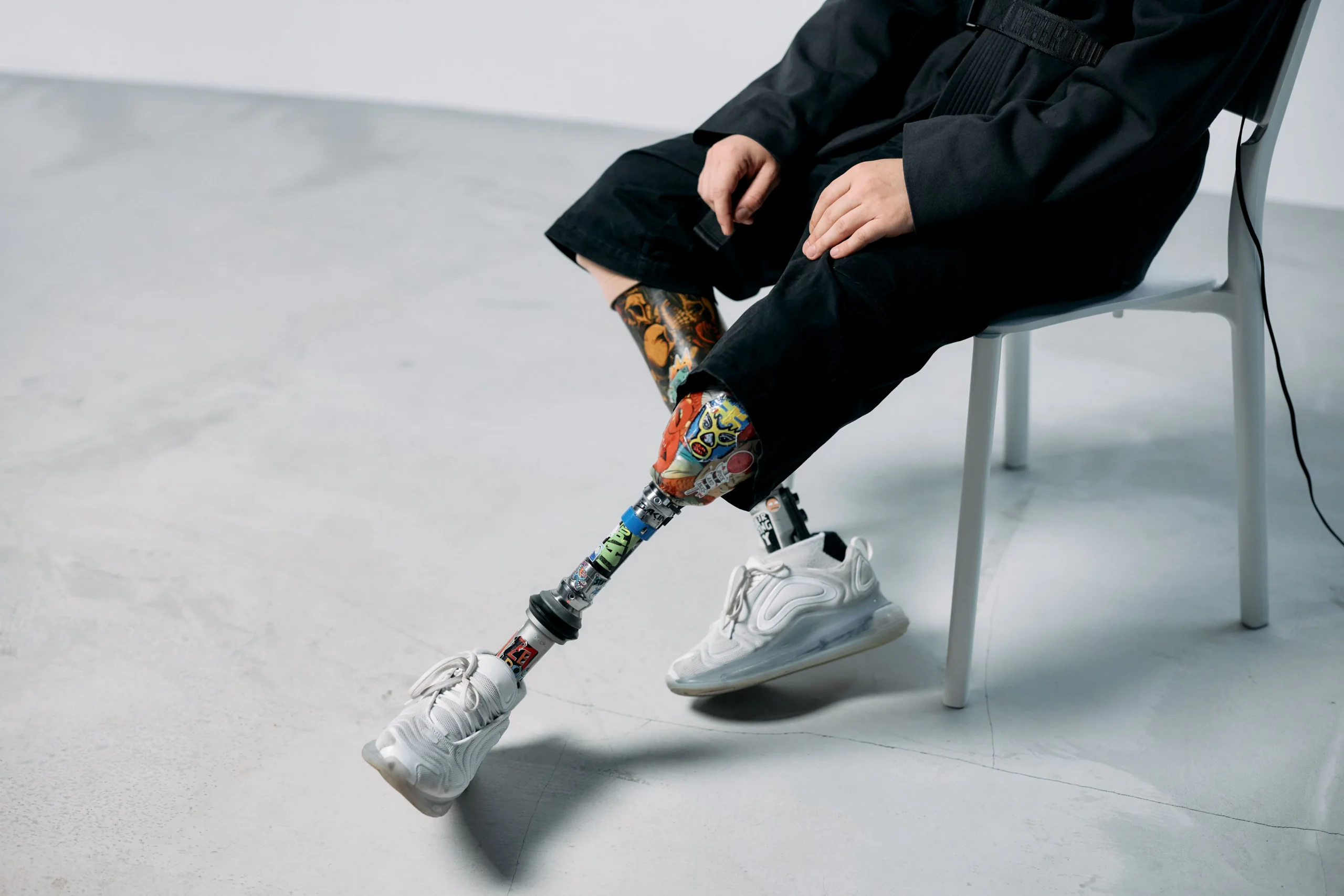 Person with a decorated prosthetic leg wearing white sneakers sitting on a chair.